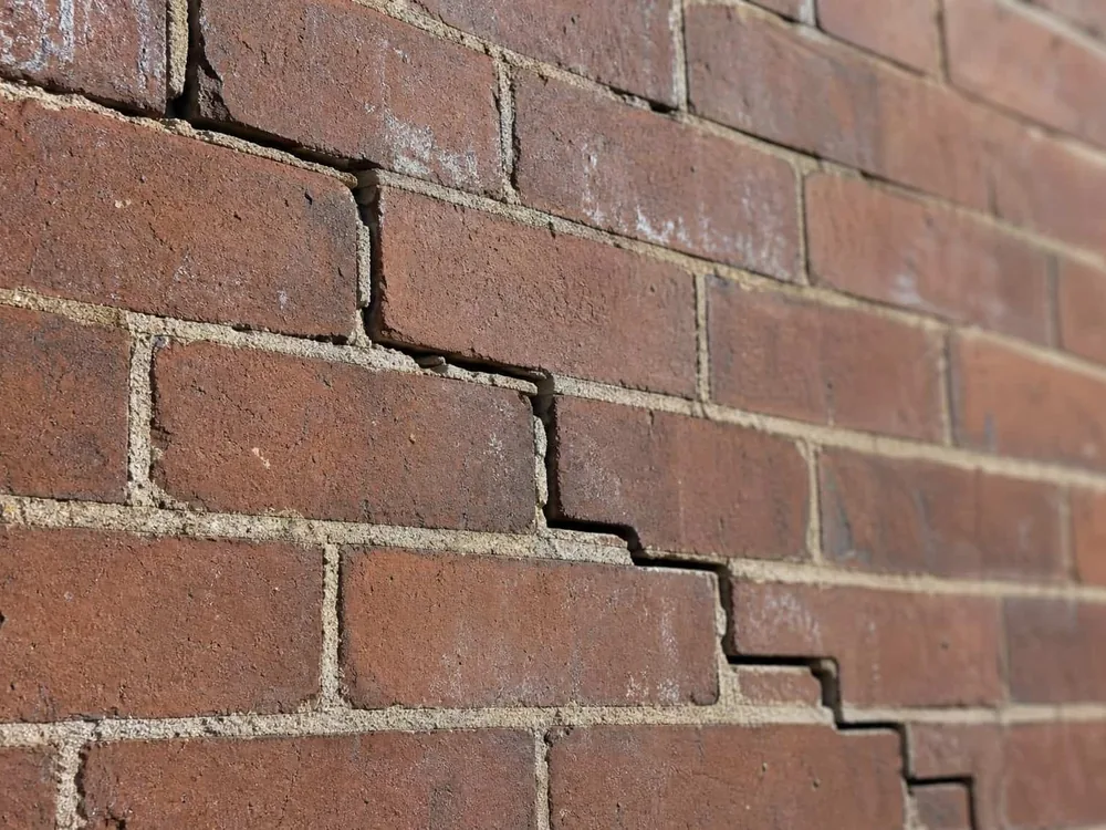 A crack in a red brick wall stepping up through the mortar joints in the staircase pattern of foundation settlement.